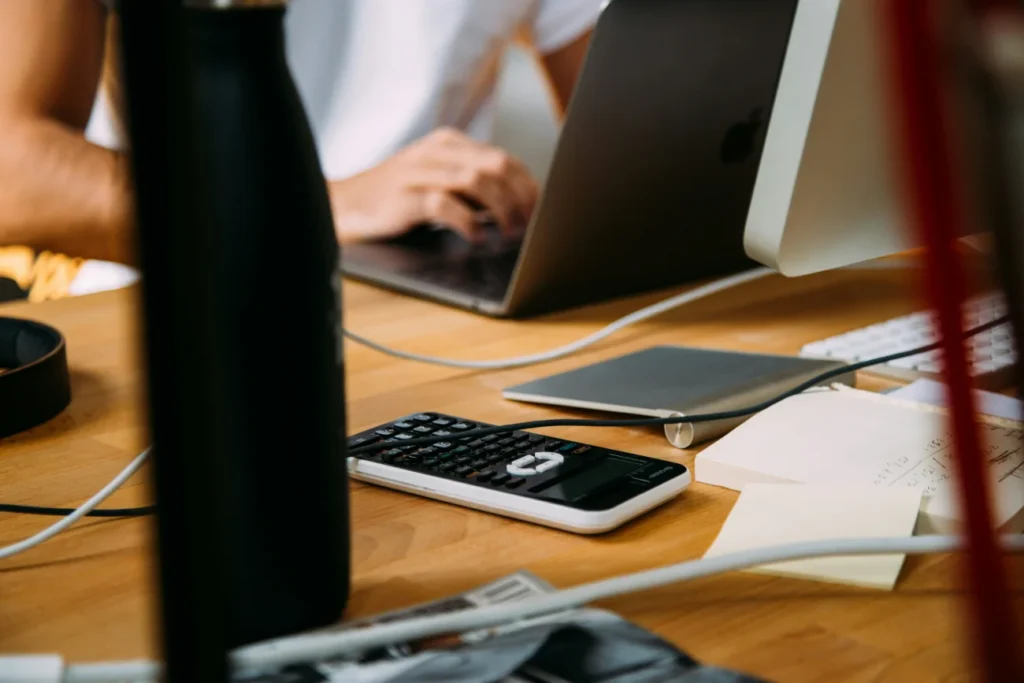 Osoba pisząca na laptopie przy biurku z kalkulatorem